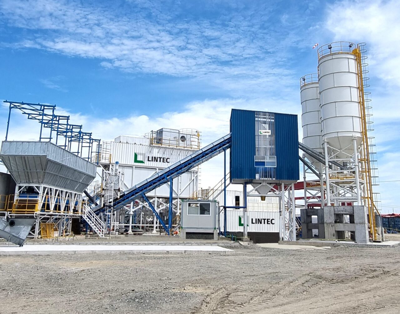 A complete Lintec concrete batching plant setup featuring aggregate hoppers, an inclined conveyor belt, a blue central mixing unit, and white storage silos